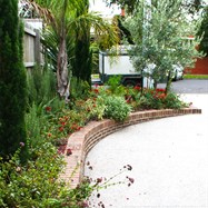   Exposed aggregate driveway, with brick retaining wall to match house planted in a Mediterranean style.